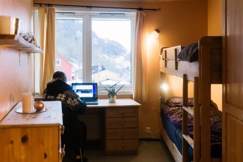 a person sitting at a desk with a laptop in a bedroom at Hardanger Hostel B&B in Lofthus