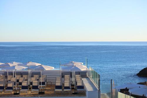 a group of umbrellas and chairs and the ocean at Mar Azul Pur Estil Hotel & Spa - Adults only in Cala Ratjada