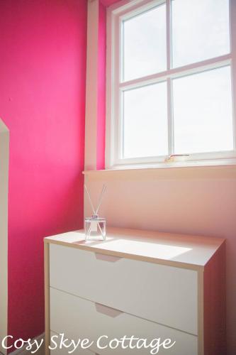 a pink room with a window and a white dresser at Cosy Skye Cottage in Kingsburgh