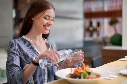 a woman drinking a bottle of water with a plate of food at Centro Capital Centre By Rotana in Abu Dhabi