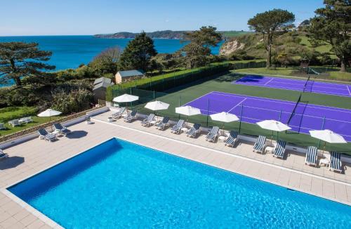 einen Blick über einen Tennisplatz mit Stühlen und einen Pool in der Unterkunft The Carlyon Bay Hotel and Spa in St Austell