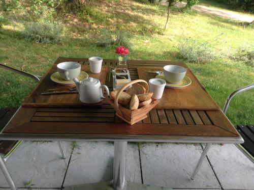 a wooden table with cups and a basket of bread at La Pierre Blanche in La Sauvetat-sur-Lède