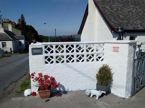 a white building with flowers and a dog next to a fence at Gumtree Cottage in Port Askaig