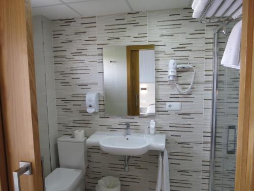 ein Badezimmer mit einem Waschbecken, einem WC und einem Spiegel in der Unterkunft Hotel La Lanzada in A Lanzada