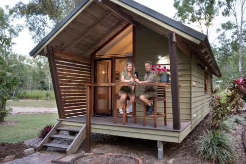 a woman sitting on a wooden bench in front of a house at Airlie Beach Eco Cabins - Adults Only in Cannonvale