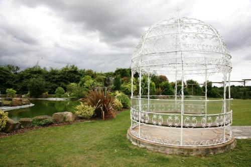 a bird cage in a garden with a pond at Manor Of Groves Hotel, Golf & Health Club in Sawbridgeworth
