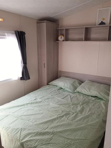 a bedroom with a bed with a green comforter and a window at Chalet Dalile IJmuiden aan Zee vlakbij het strand in IJmuiden