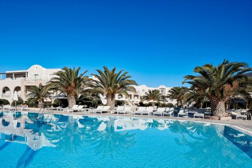 a large swimming pool with palm trees and chairs at Santo Miramare Beach Resort in Perivolos