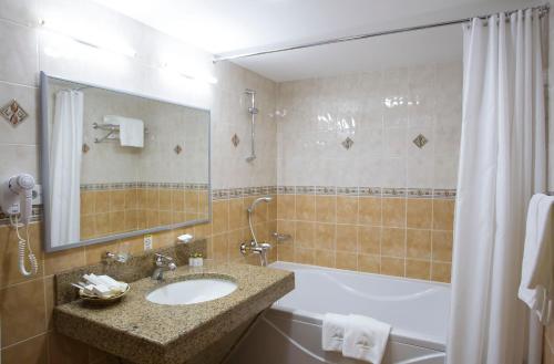 y baño con lavabo, bañera y espejo. en Atyrau Dastan Hotel en Atyraū