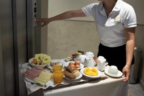 a woman standing next to a table with a tray of food at Albergo Belsoggiorno in Sanremo