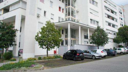 a white building with cars parked in a parking lot at Inci apartman in Pécs