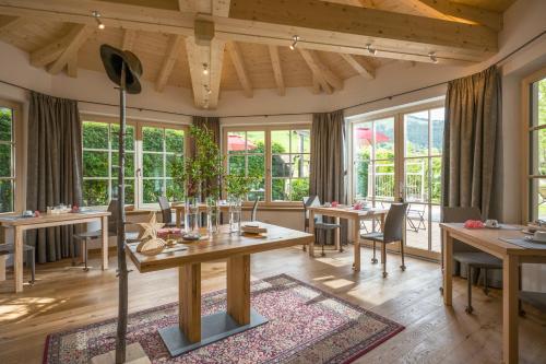 a dining room with tables and chairs and windows at Flora - Das kleine Gartenhotel in Ellmau
