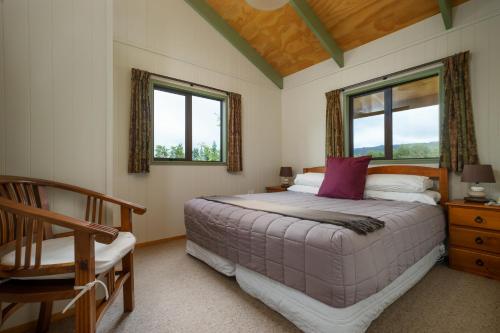 a bedroom with a bed and a chair and two windows at Longbourne Lodge Motel Mosgiel in Mosgiel