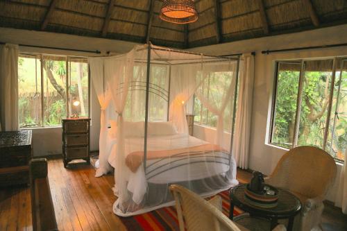 a bedroom with a canopy bed in a room with windows at Phophonyane Falls Ecolodge in Piggs Peak