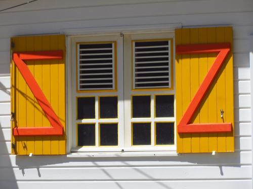 a window with yellow and red shutters on a house at Residence Hôteliere Hurlevent in Grande Anse