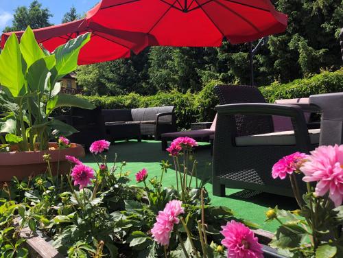 patio z czerwonym parasolem, krzesłami i kwiatami w obiekcie Willa Słoneczna w Okunince