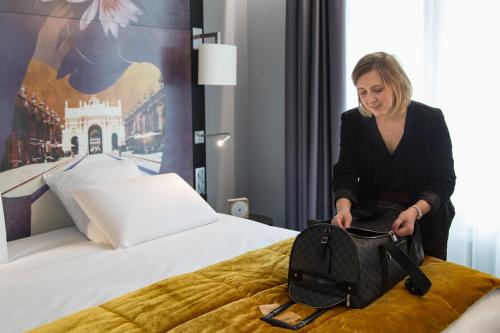 a woman sitting on a bed with a bag at Mercure Nancy Centre Place Stanislas in Nancy
