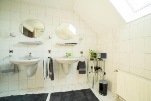 ein weiß gefliestes Bad mit 2 Waschbecken und einem Spiegel in der Unterkunft Gästehaus Marichen in Aurich
