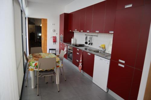 cocina con armarios rojos, mesa y sillas en Costa Apartments, en Ponta Delgada