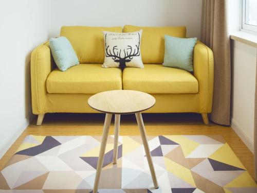 a yellow couch with a stool in a living room at Shell Shanghai Jiadingbei Subway Station Shuping Road Hotel in Xuhang