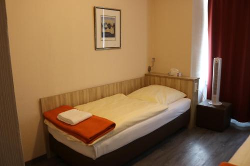 a small bedroom with a bed with an orange blanket on it at Hotel Paris in Düsseldorf