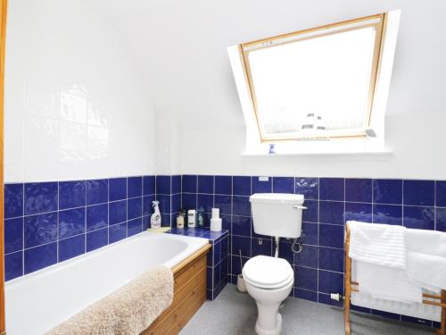 a blue tiled bathroom with a toilet and a tub at Dunnottar Woods House in Stonehaven