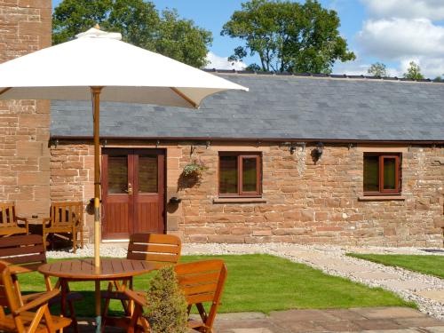 a table with an umbrella in front of a building at Daisy Cottage in Penrith