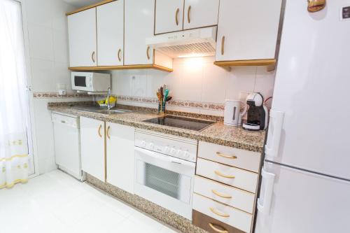 La cuisine est équipée de placards blancs et d'un réfrigérateur blanc. dans l'établissement Nations Apartment with pool, à Alicante