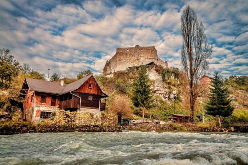 a house with a castle on a hill next to a river at Apartments Strmac in Slunj