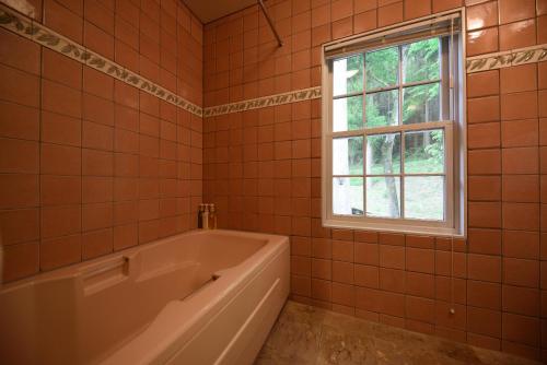 an orange tiled bathroom with a tub and a window at Yufuin Hotel Mori-no-Terrace in Yufuin