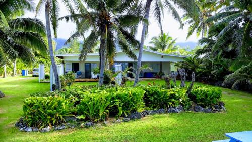 a house with palm trees in front of a yard at Herons Reef Holiday Apartments in Rarotonga