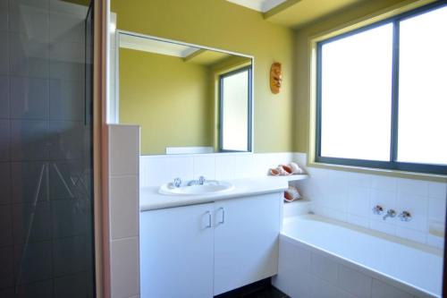 a bathroom with a sink and a tub and a mirror at BEACHCROFT - INLET SIDE in Inverloch