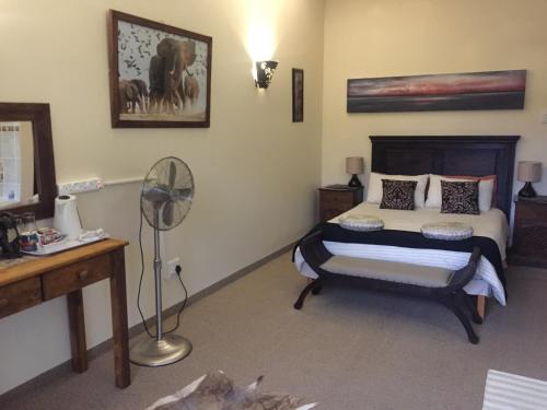 a bedroom with a bed and a desk and a fan at Cheetah Lodge Guest House in Hartenbos