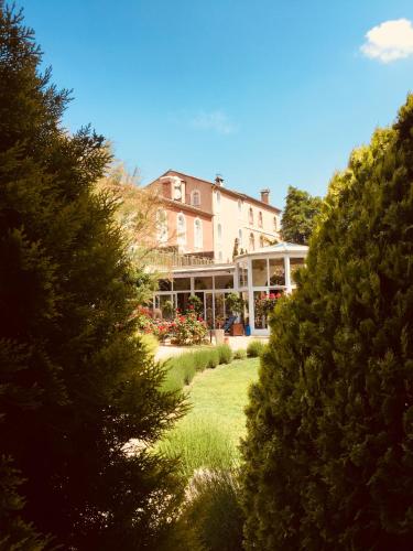 a large house behind some trees and a yard at Moulin de la Roque in Althen-des-Paluds