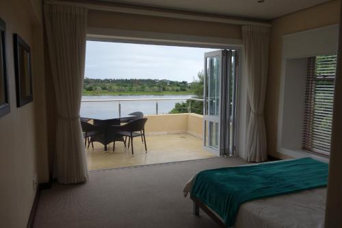 1 dormitorio con 1 cama y balcón con mesa y sillas en Twin Rivers Villa, en Plettenberg Bay