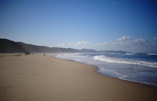 a beach with people walking on the sand and the ocean at Dune View Cottage in Sodwana Bay