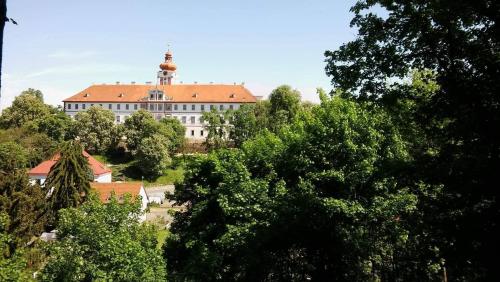 a large white building with a red roof behind trees at Chalupa pod zámkem in Mnichovo Hradiště