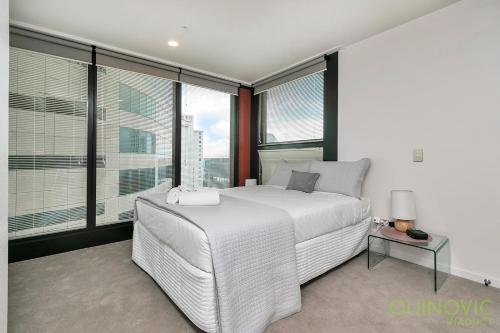 a bedroom with a white bed and large windows at QV Stays Spacious City Getaway in Auckland