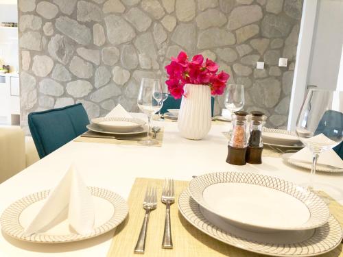 una mesa con platos y un jarrón con flores rosas en Colours Seaview Apartment, en Néa Artáki