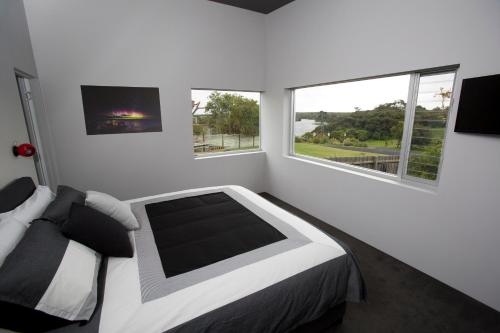 a white bedroom with a bed and two windows at Nelson Victoria Luxury Holiday Accommodation in Nelson