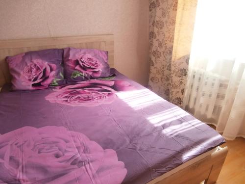 ein Bett mit lila Laken und rosa Rosen darauf in der Unterkunft Apartments at the church alley in Daugavpils