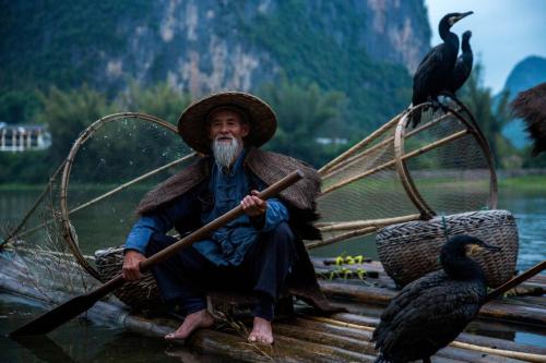 a man is sitting on a boat with an oar at Li-river Island Resort Xingping Yangshuo in Yangshuo