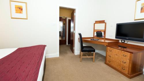 a hotel room with a desk with a television and a bed at Pitbauchlie House Hotel - Sure Hotel Collection by Best Western in Dunfermline