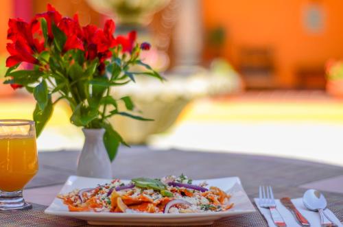 a plate of food on a table with a vase with red flowers at Hotel Diego de Mazariegos in San Cristóbal de Las Casas