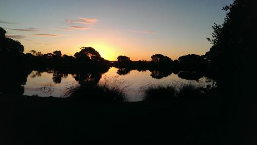 a sunset over a lake with trees in the background at Stanley Lakeside Spa Cabins in Stanley
