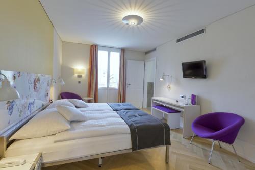a bedroom with a bed and a desk and purple chairs at Boutique Hotel Bellevue in Interlaken