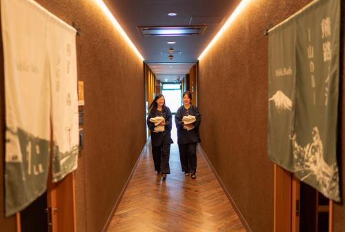 two women walking down a hallway with signs on the walls at Hotel Torifito Otaru Canal in Otaru