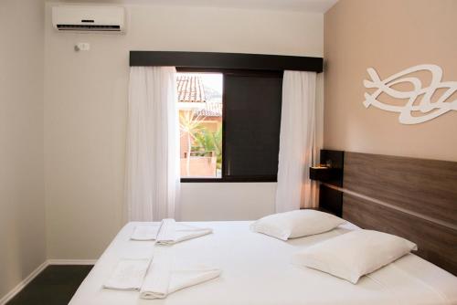 1 dormitorio con 2 camas con sábanas blancas y ventana en Pousada Larimor en Boicucanga