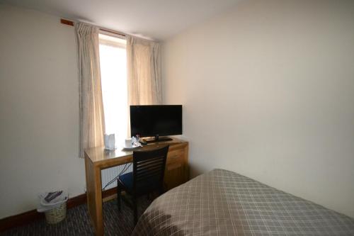 a bedroom with a desk with a bed and a television at Airport Guest House in Slough