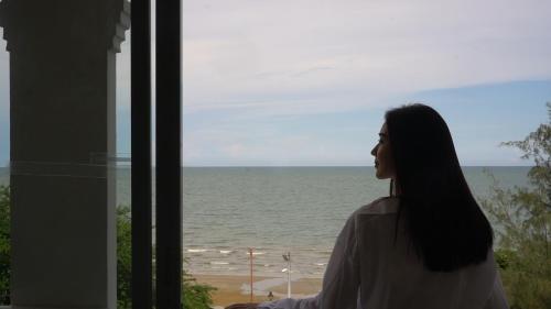 a woman looking out a window at the ocean at Talay Hotel and Villa Cha-am in Cha Am